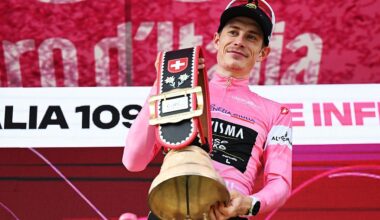 Jonas Vingegaard in the pink jersey on the podium holds a huge bell as prize by the Swiss hosts