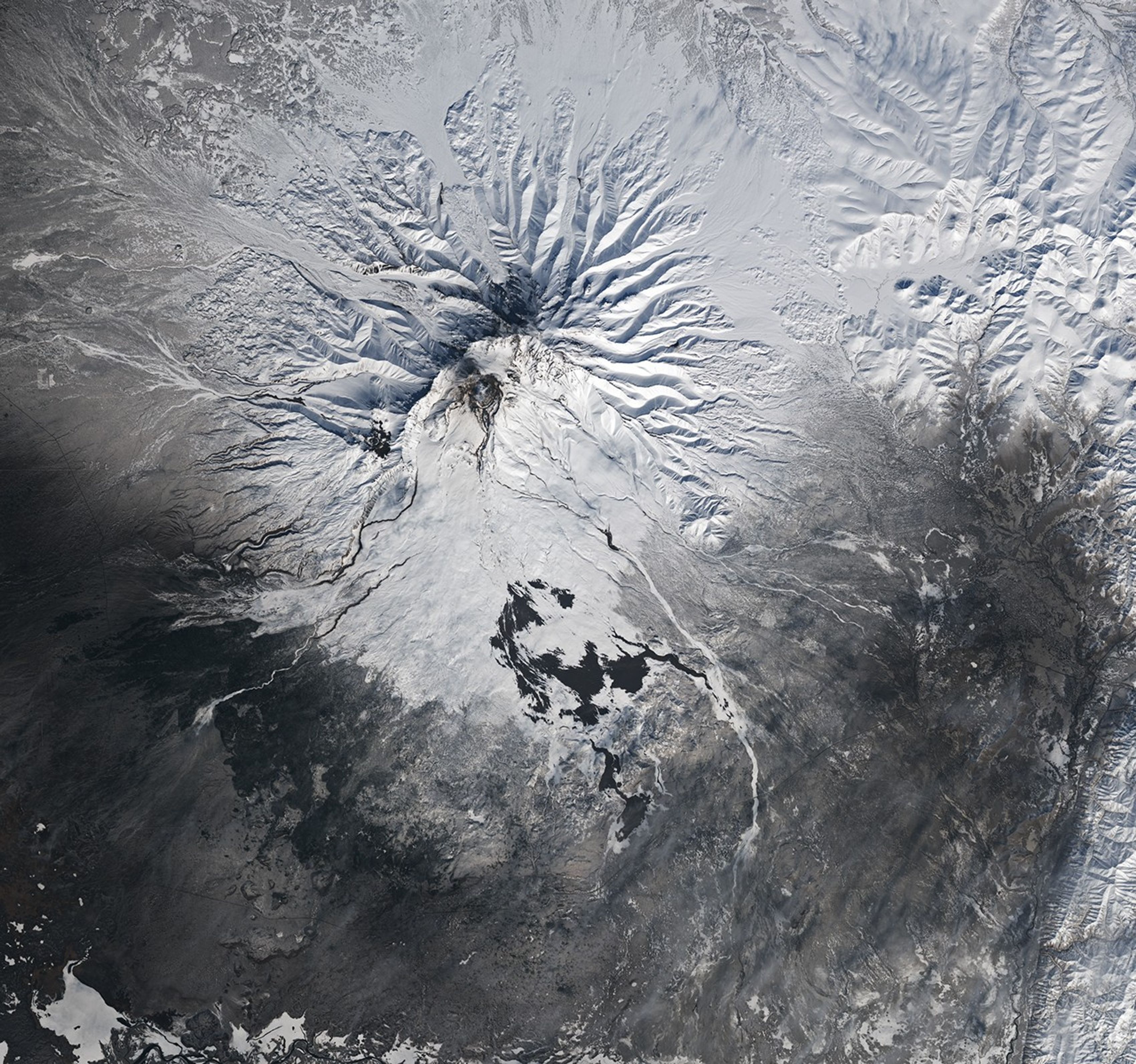 Dark channels and volcanic deposits are visible on the slopes of the snow-covered mountain.