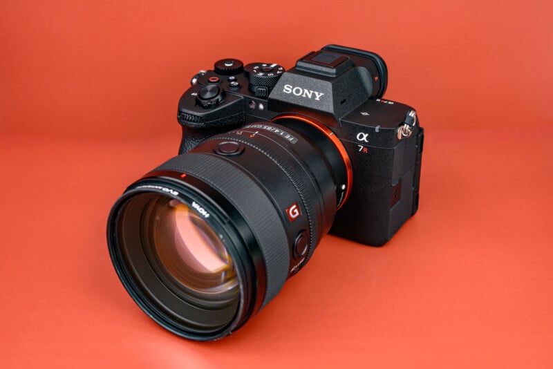 A black Sony α7R mirrorless camera with a large Sony G Master lens is displayed on an orange background.