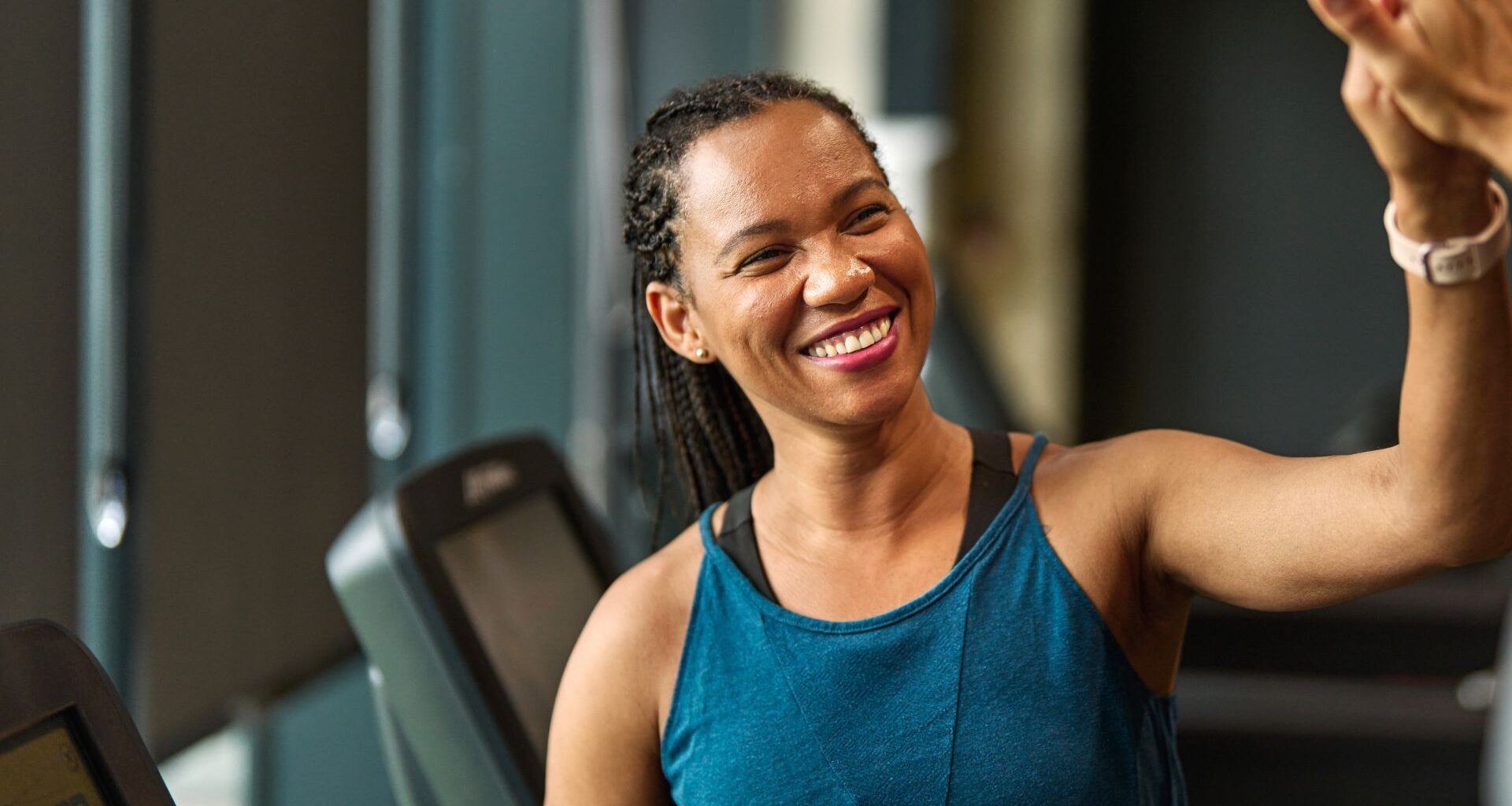 Woman high fiving after doing treadmill workout, smiling and wearing workout clothes