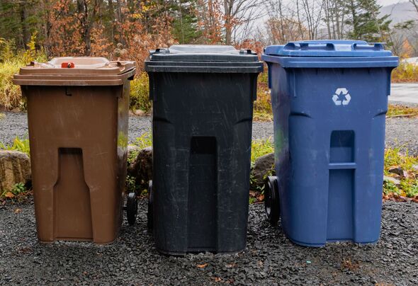 Three Outdoor Recycling and Trash Bins Lined Up On Gravel Near Trees and Road Three Outdoor Recycling and Trash Bins Lined Up On Gravel Near Trees and Road