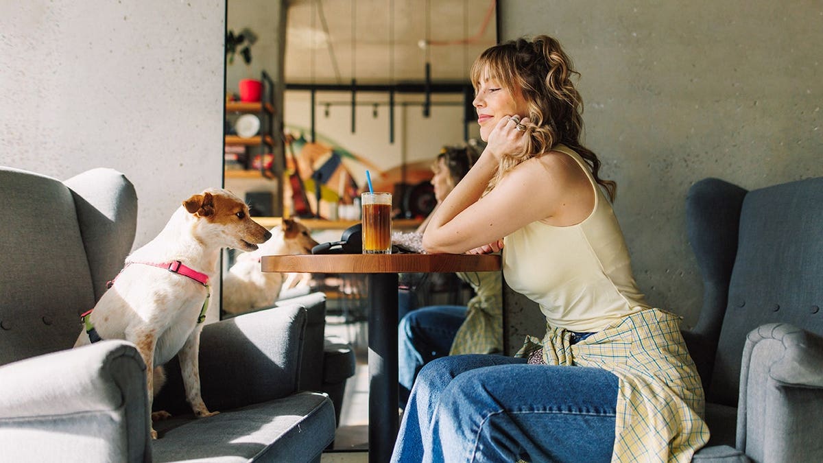 A woman sitting at a café table with her dog beside her