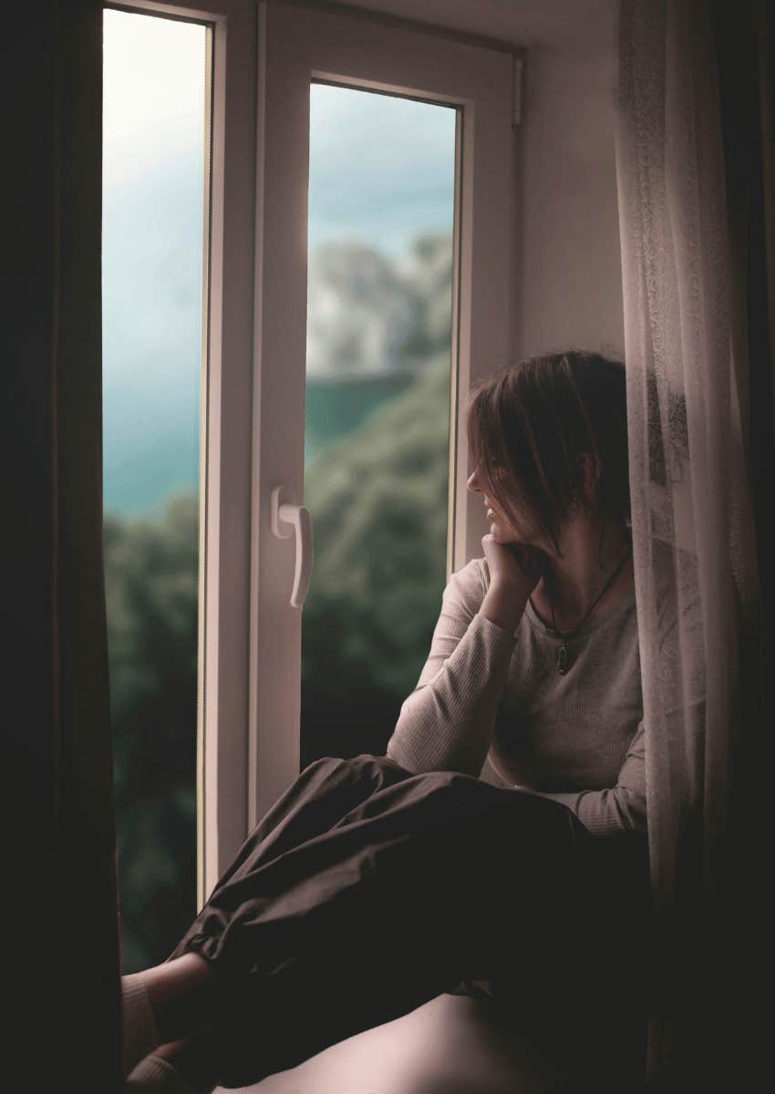 woman sitting alone at window on cloudy day