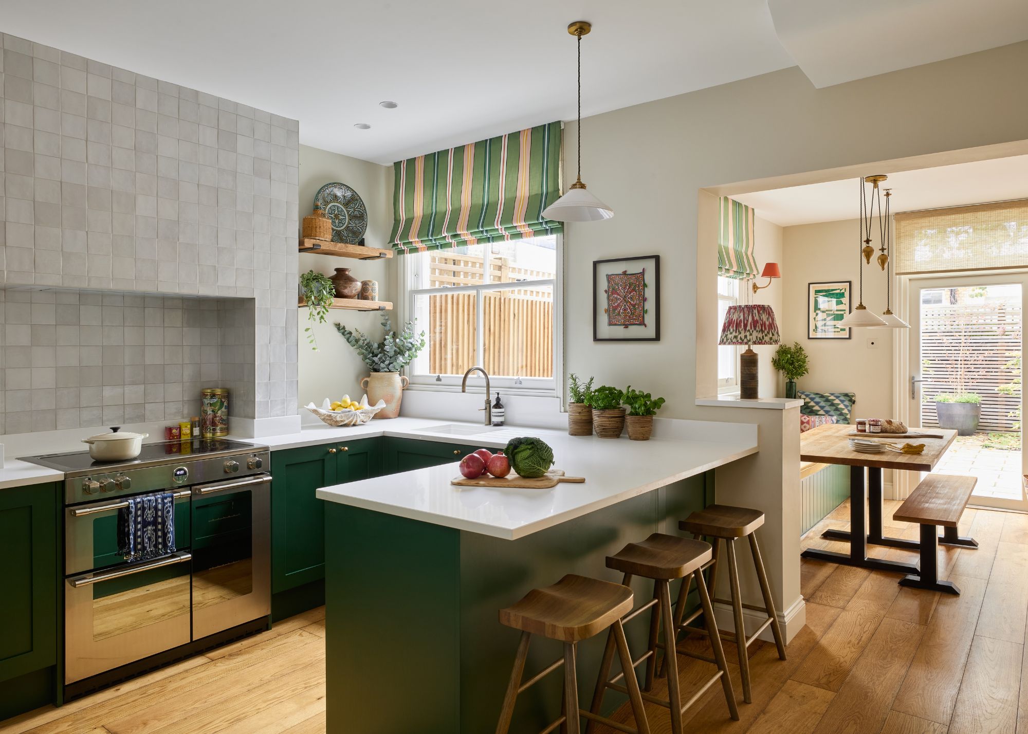 A modern kitchen with neutral walls, wooden flooring, and dark green lower cabinets, and an island with white counters. A large oven with gray tiles above it and a doorway leading into a dining room.