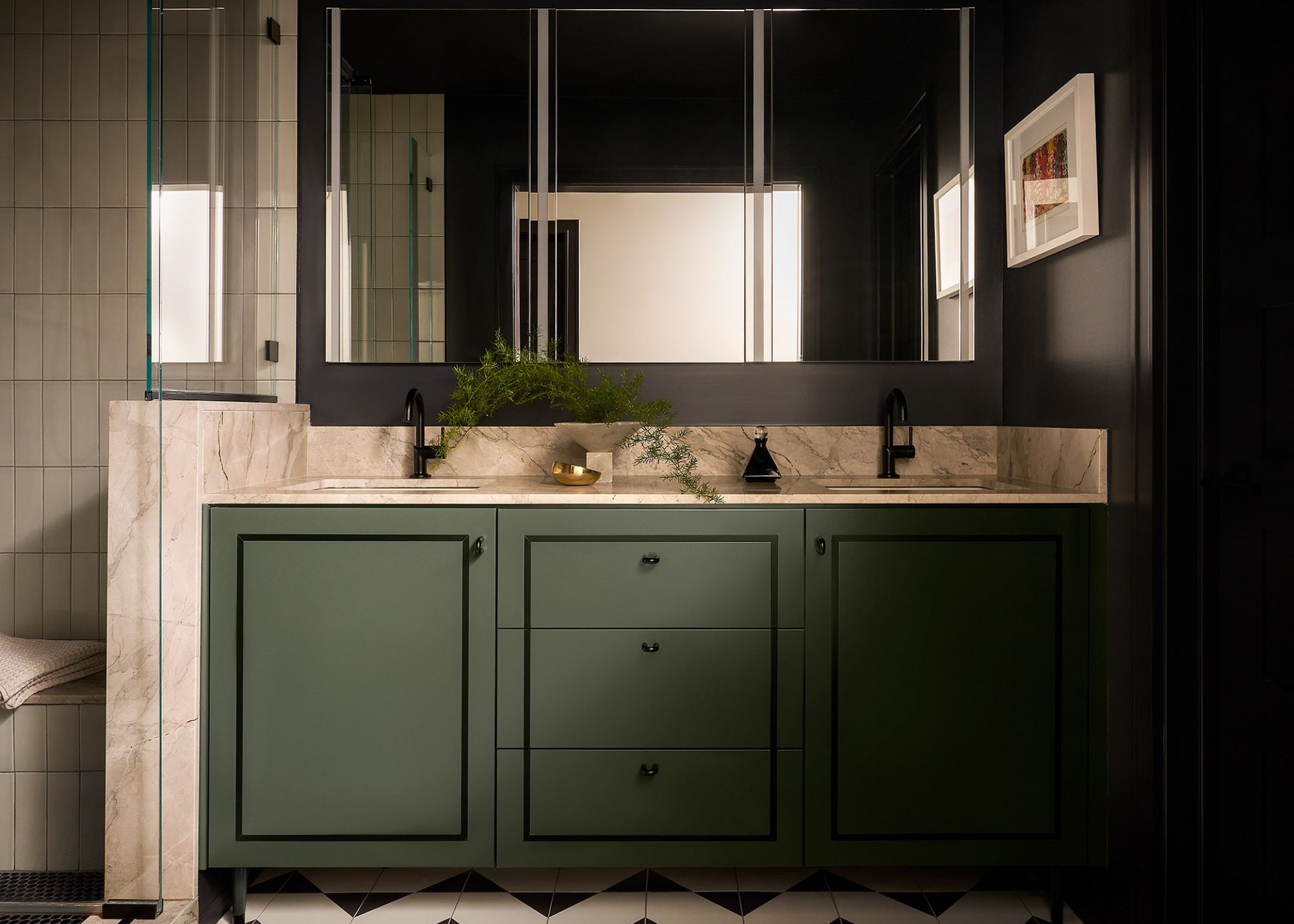 A modern bathroom with dark green cabinets, marble countertops, a mirrored wall cabinet, and black walls.