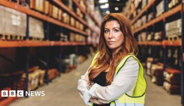 Woman in a warehouse with red hair and a hi-vis jacket.