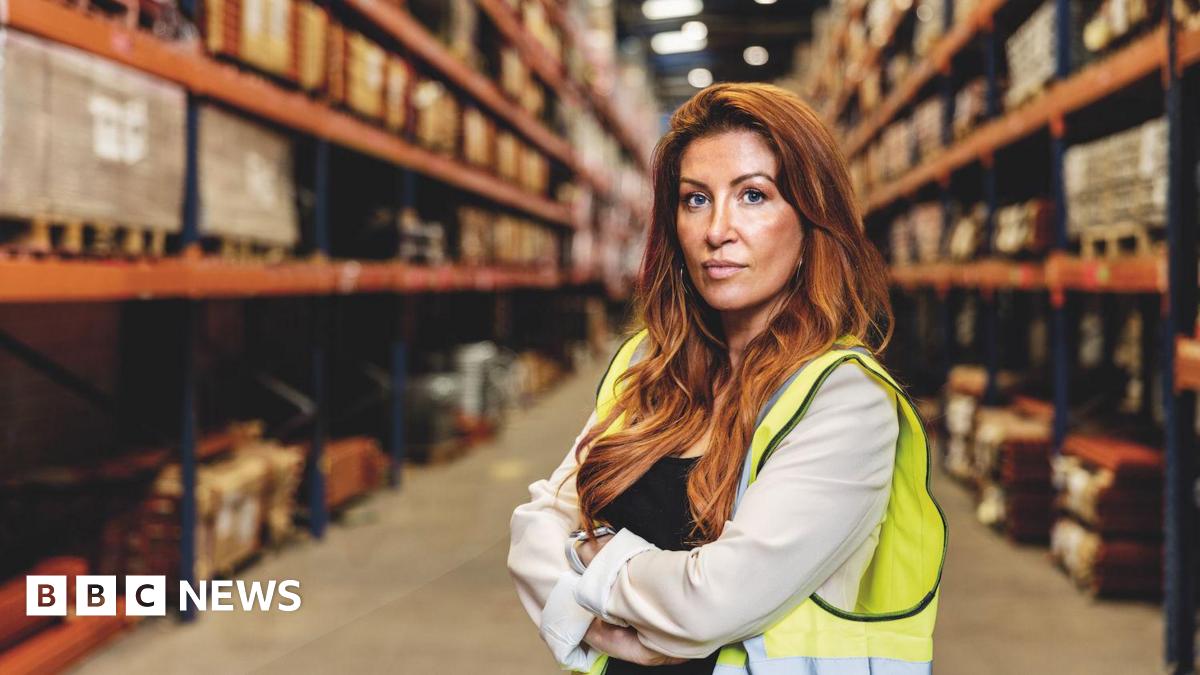 Woman in a warehouse with red hair and a hi-vis jacket.