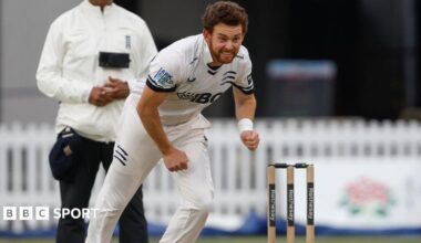 Middlesex's Ryan Higgins, in whites, completes his bowling action with stumps and umpire visible