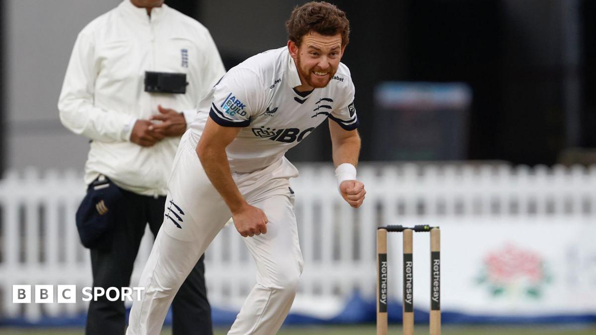 Middlesex's Ryan Higgins, in whites, completes his bowling action with stumps and umpire visible