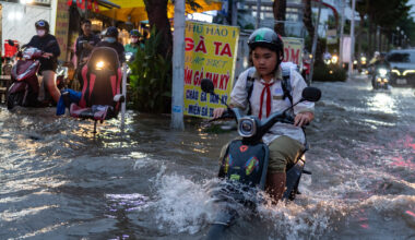 A person drives a motorbike through a flooded street.