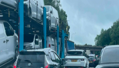 A queue of mainly black and white cars and a car transporter on a motorway