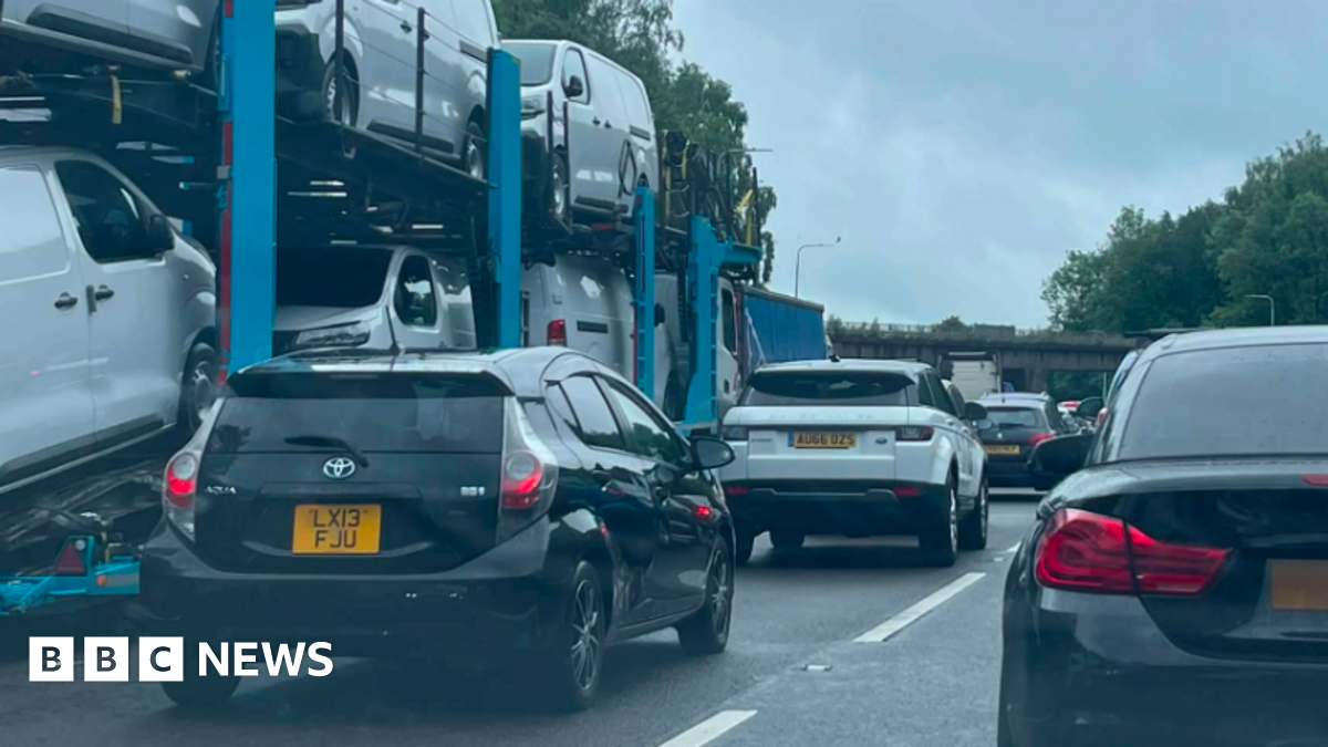 A queue of mainly black and white cars and a car transporter on a motorway