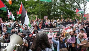 A large group of protesters outside Woolwich Crown Court. Many of them are holding flags and banners in support of Palestine Action.