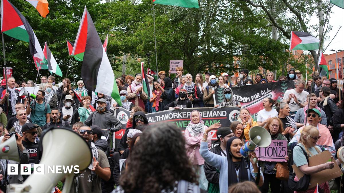 A large group of protesters outside Woolwich Crown Court. Many of them are holding flags and banners in support of Palestine Action.