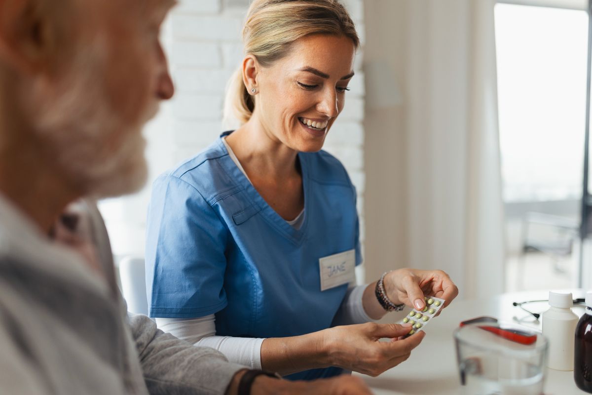 Nurse helping senior man with medication administration, explaining dosages and timing of intake. Ill man taking prescribed medication, reading the label on the bottle.