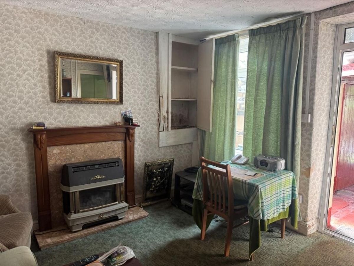 Inside the rear reception room with dated 1970a fireplace, small cream sofa and small dining table and chairs of Last house on the streets of village of Troedrhiwfuwch going to auction with guide price of £35k plus with Paul Fosh Auctions