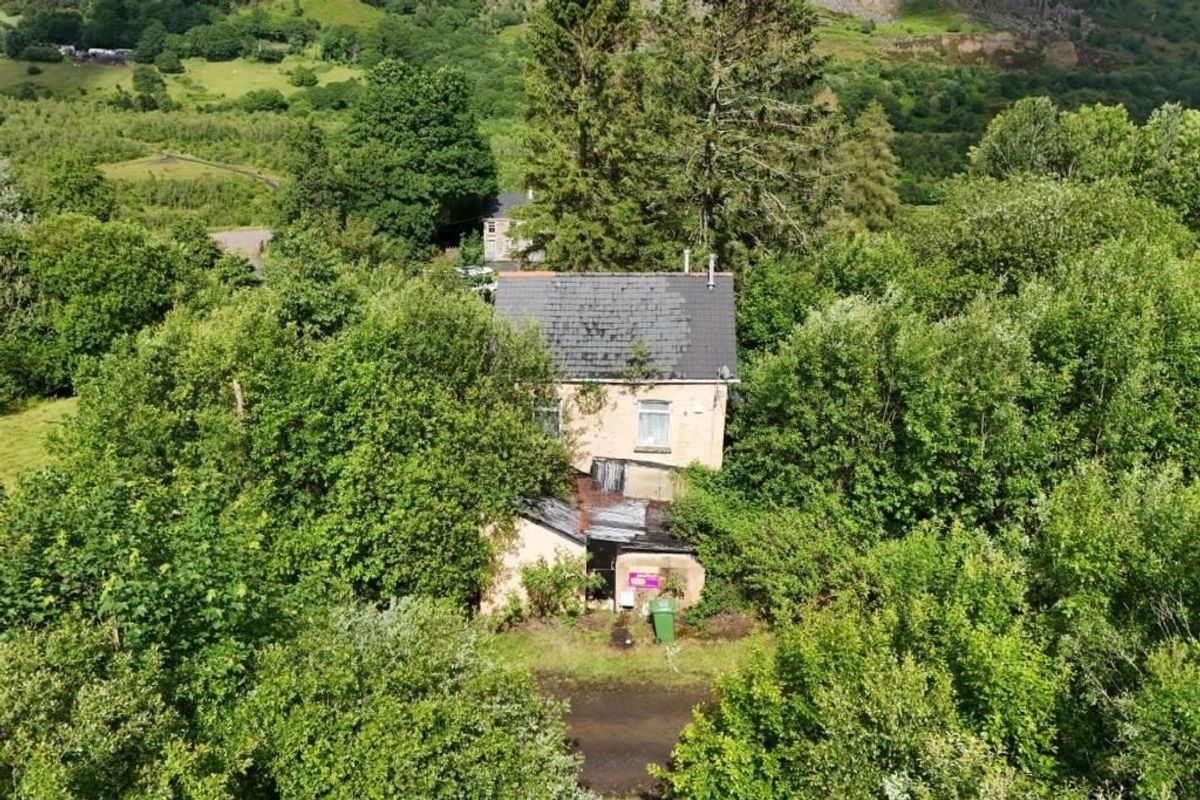 Aerial view of Last house on the streets of village of Troedrhiwfuwch going to auction with guide price of £35k plus with Paul Fosh Auctions surrounded by trees