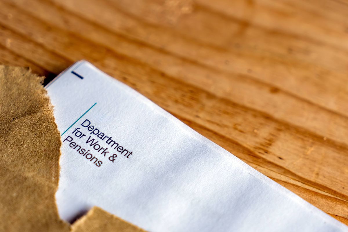 A torn brown envelope lies open on a wooden table, exposing a white letter inside detailing a state pension increase of 5% effective from 6 April 2016, with references to payments starting 5 May 2020. The document includes official formatting and text about pension adjustments. This image captures a straightforward financial notice in a simple indoor setting, suitable for illustrating articles on retirement benefits, government policy changes, or personal finance updates in media publications. It can be used in contexts like news stories on social security, economic reports, or advisory content for seniors planning finances.