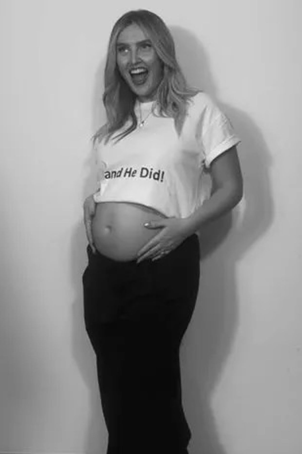 Perrie holding her baby bump and smiling in a black and white photo
