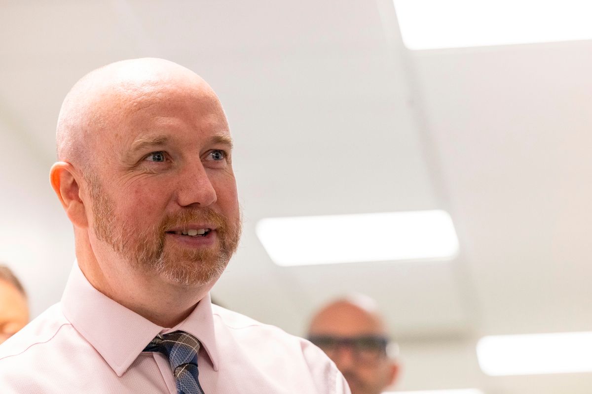 A man in a tie and shirt smiling while speaking in a hospital corridor