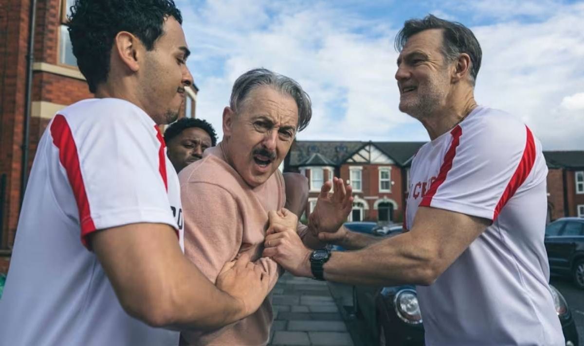 Men wearing football shirts grabbing at a man with a moustache