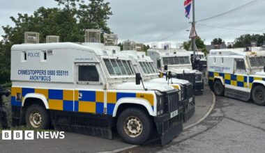 A number of Police Service of Northern Ireland landrovers are seen parked up beside a bridge in the village of Scarva ahead of the arrival of a Palestine solidarity parade. A Union Jack flag can also be partially seen at the top of the picture attached to a lamp post.