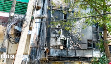 Firefighters and police officers stand at the site after a fire at a hotel in New Delhi