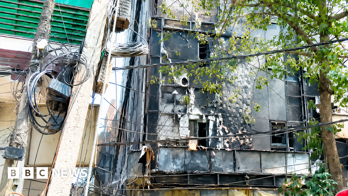 Firefighters and police officers stand at the site after a fire at a hotel in New Delhi