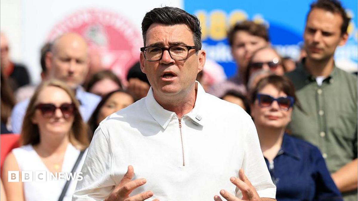 Andy Burnham delivering speech outside in sunny weather in white collared top with zip closure and people behind in sunglasses