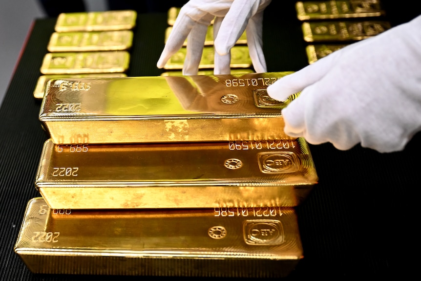 Two hands with white gloves handle gold bullion