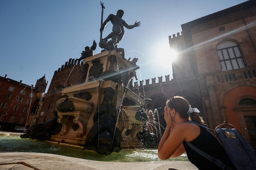 A woman splashes water on her face from a large fountain in the shape of Neptune.