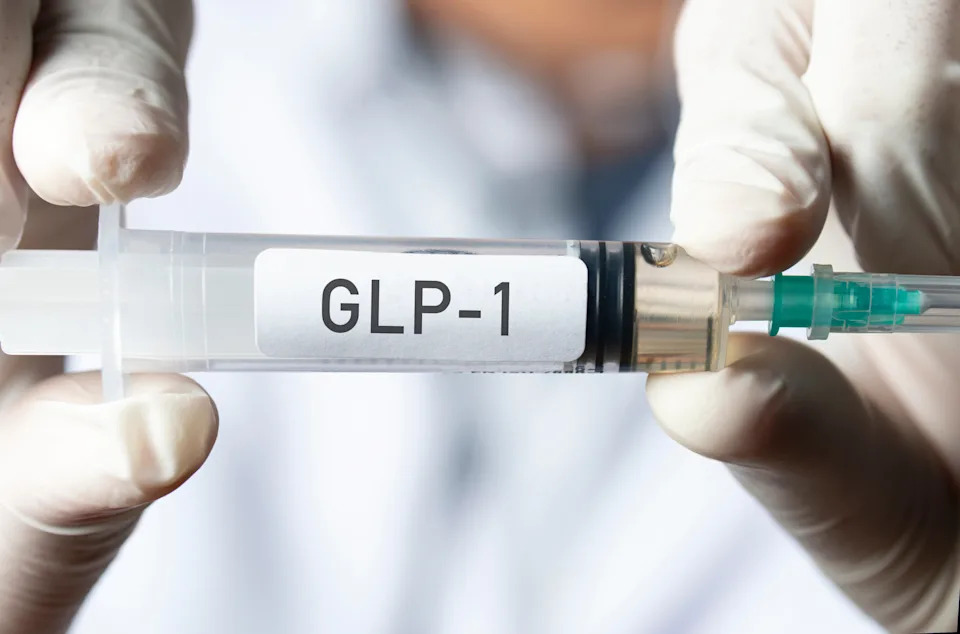 Hands holding a syringe labeled "GLP-1," representing a medical treatment or medication related to health