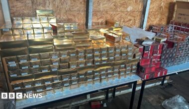 Stacks of gold packages and red packages which look to be perfume packaging stacked on a table.