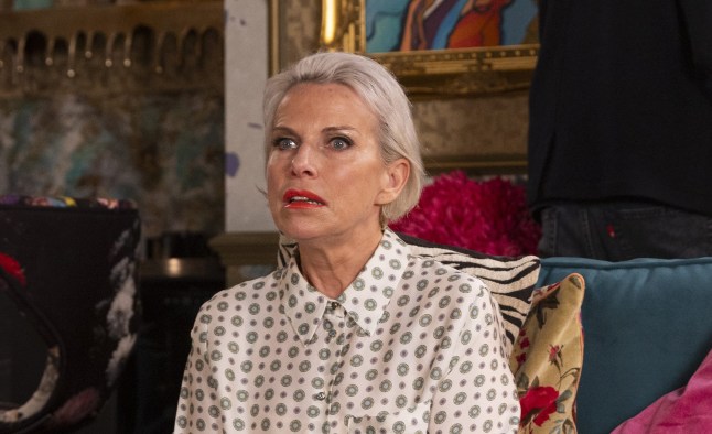 A wide-eyed Debbie Webster looking stunned while sitting on a sofa in Coronation Street.