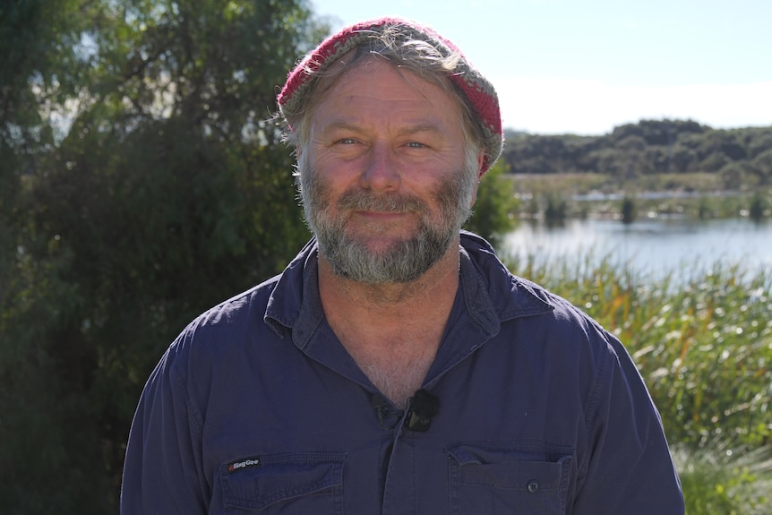 Tim Gamblin wears a blue shirt and a red and grey knitted hat. The wetlands in the background.