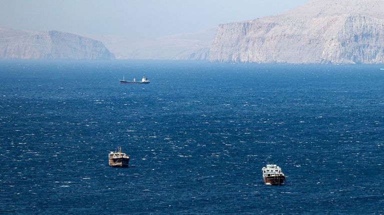 Oil tankers in blue waters set against cliffs.