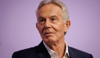 Tony Blair delivering a speech at a conference podium, discussing current global political issues.
