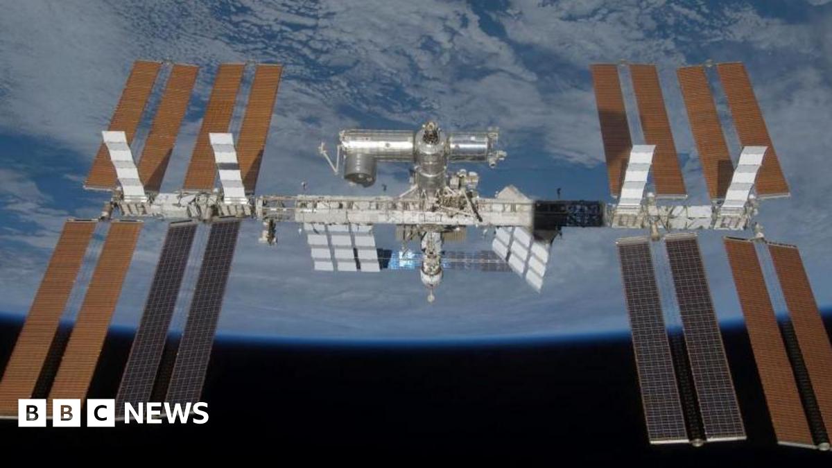 The International Space Station is seen in the centre of the image in space orbiting the Earth