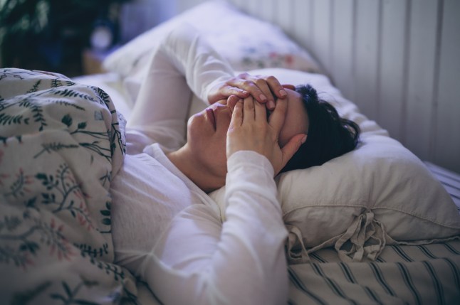 Sleepless young woman suffering from insomnia, covering eyes with hands