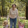 Laura Terry stands in between her two daughters, who are seated on a swing set.