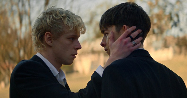 Leviticus still: two teen boys, the blonde cradling the cheek of the brunet, both in suits.