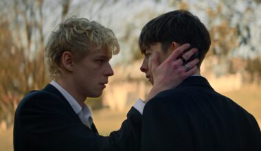 Leviticus still: two teen boys, the blonde cradling the cheek of the brunet, both in suits.