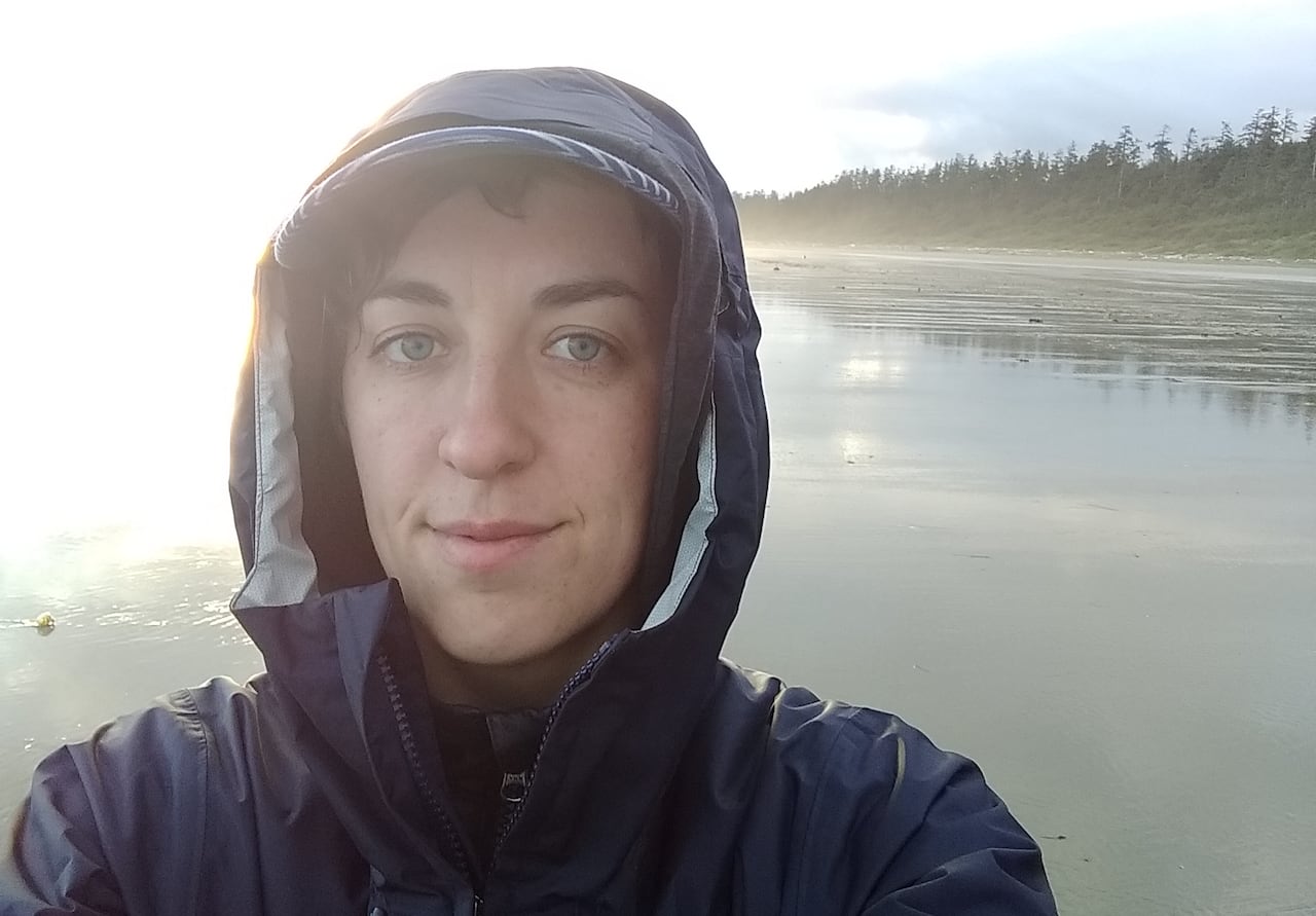 A selfie of a woman in a hooded jacket with a body of water behind her.