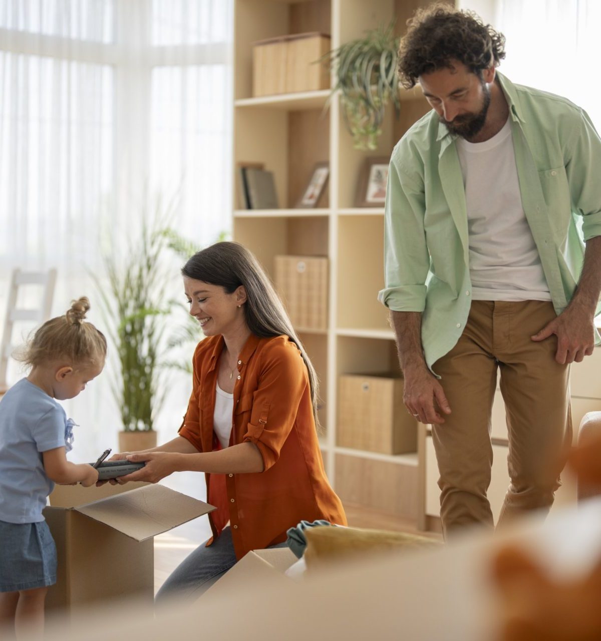 Parents and young child moving into a new house, unpacking belongings from cardboard boxes