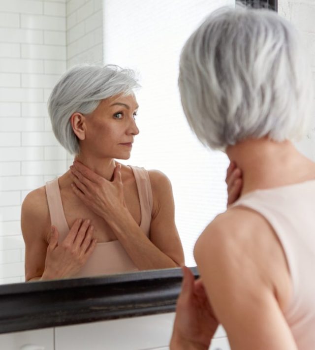 Closeup portrait of gorgeous happy middle age woman looking at mirror touching her skin enjoying treatment for dry skin. Advertising of antiaging beauty skin care products