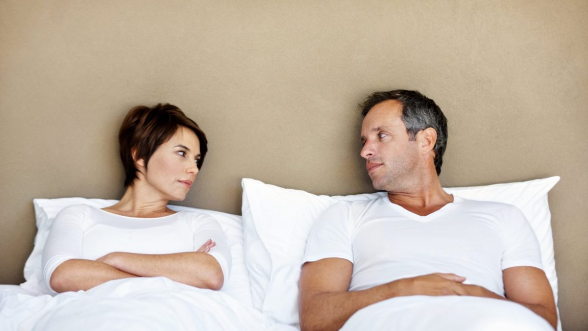 A mature couple sitting in bed and looking at each other angrily after a disagreement