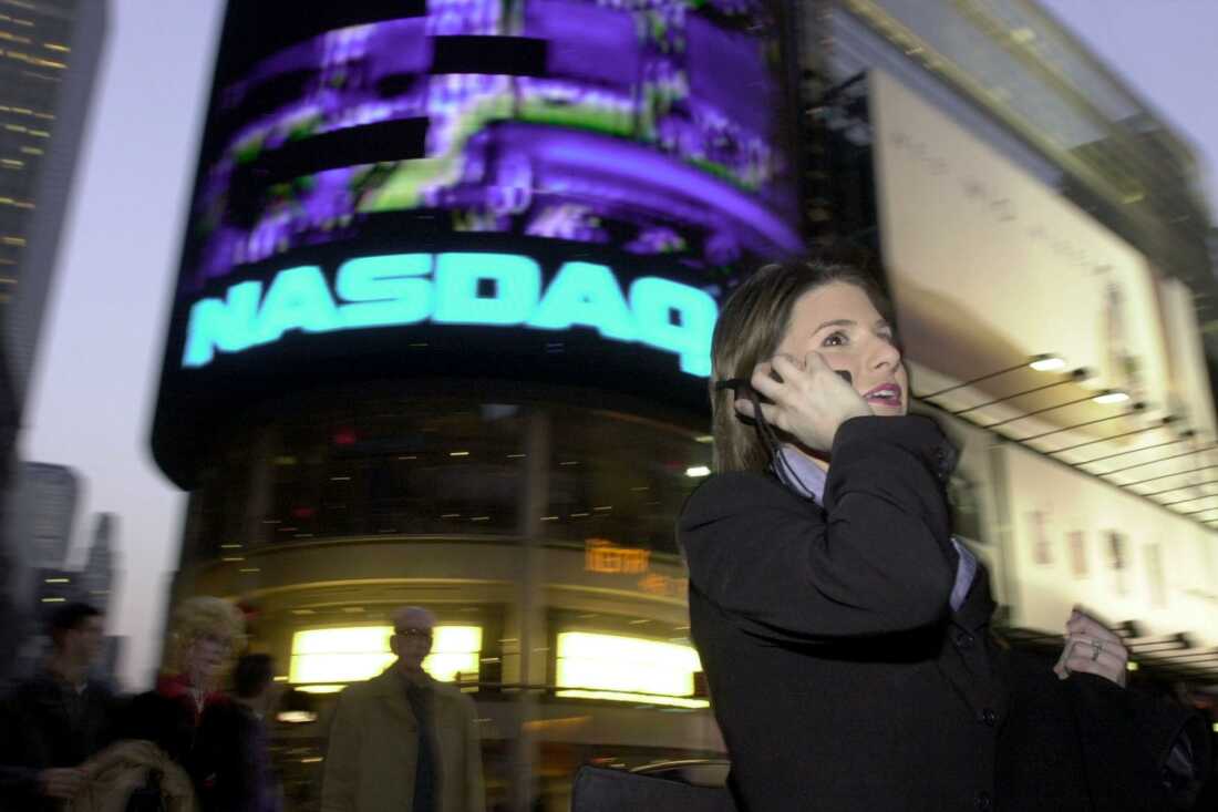 In this photo from 2000, a woman holding a cellphone to her ear walks past the illuminated Nasdaq sign in New York City's Times Square.
