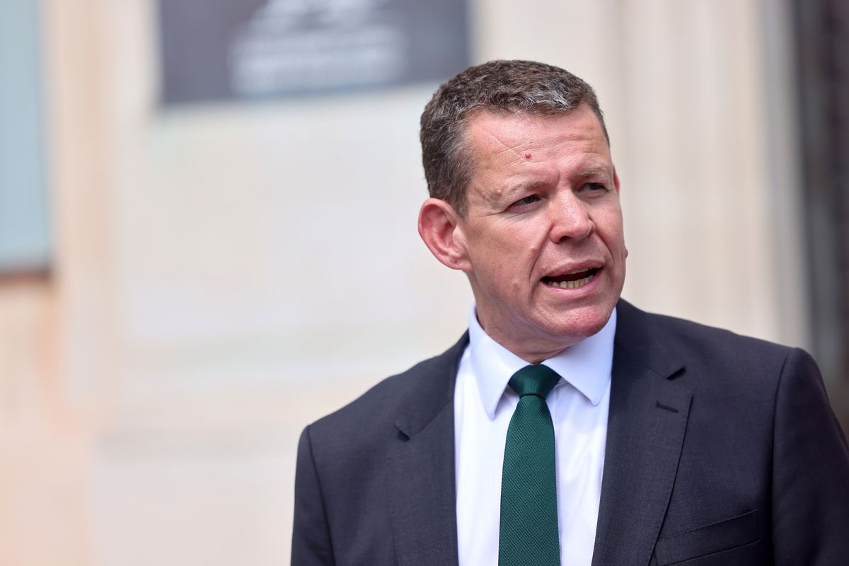 A man in a dark suit and green tie mid sentence