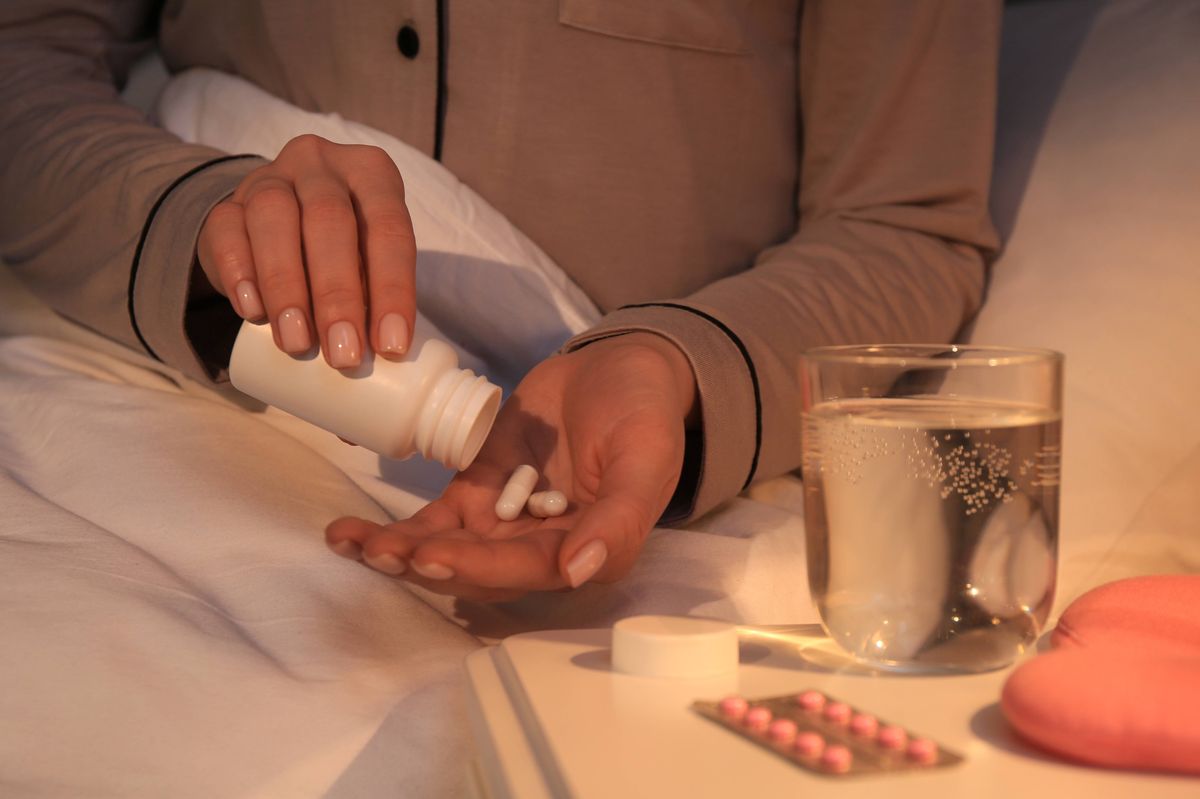 Woman pouring pills from bottle into hand indoors, closeup.