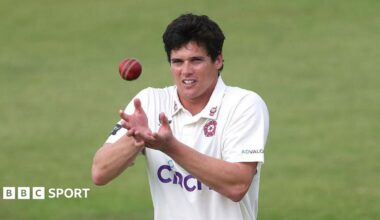 Liam Guthrie, wearing a white Northamptonshire shirt, cups his hands ready to catch the red cricket ball